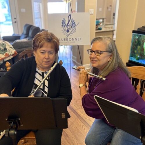 Two women holding flutes, looking at music together on a black music stand